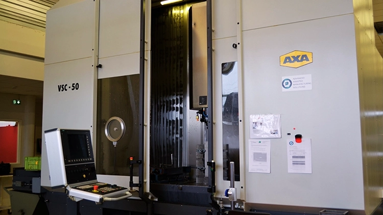 Three-quarter view of the AXA VSC-50 machine, powered off, with the right-hand door open and the control panel beside it, in a metallurgical R&D workshop.