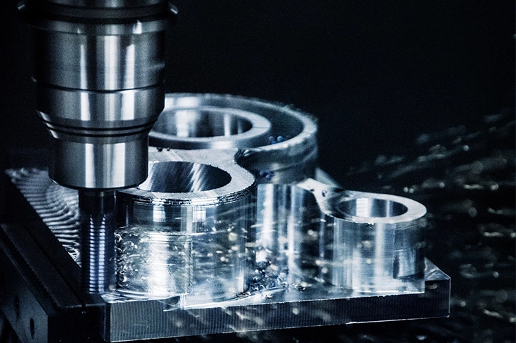 Close-up view of a cutting tool in contact with a silver-coloured workpiece, with lubricant being sprayed in droplets between the cutting tool and the workpiece.