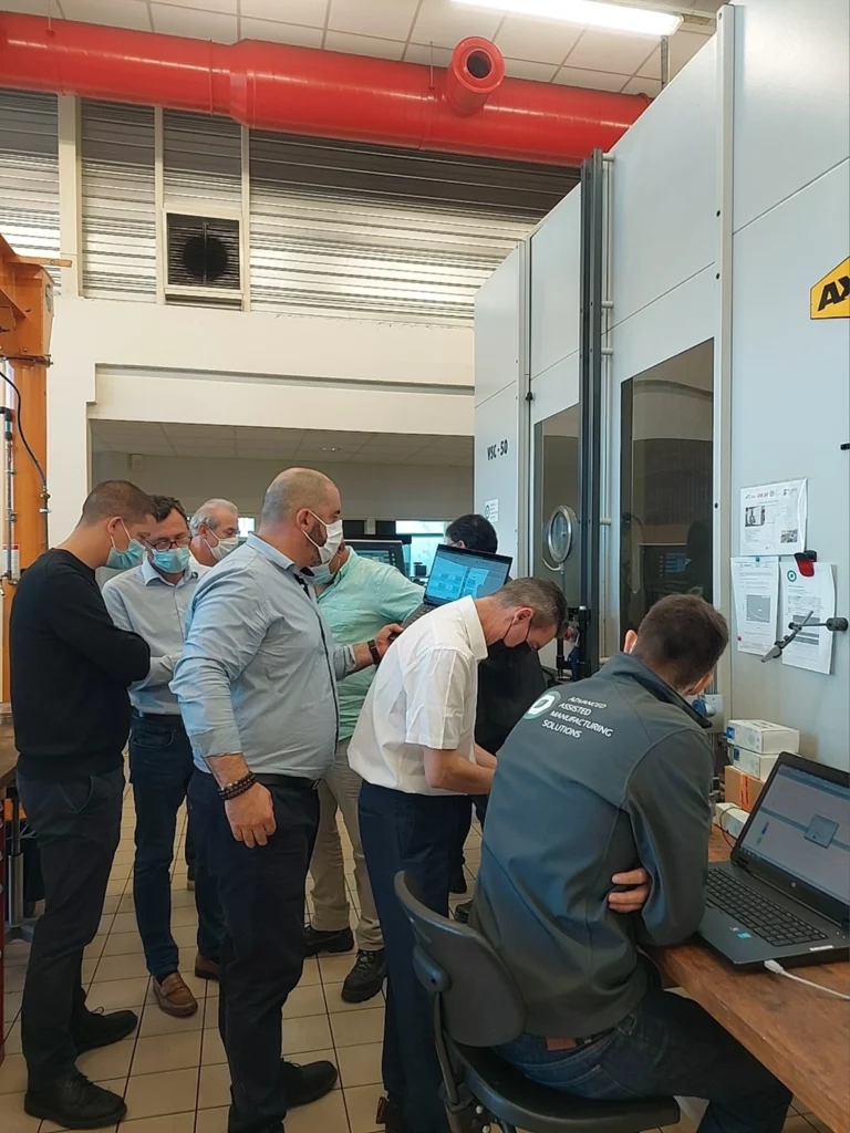 Linear perspective view of the AXA VSC - 50, with clients in front of it in the metallurgical R&D workshop participating in a technical day.